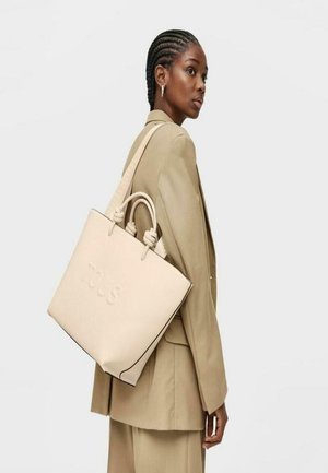 Borsa tote in pelle beige con doppio manico superiore, logo stampato sul davanti e bordature nere a contrasto, presentata su uno sfondo neutro.