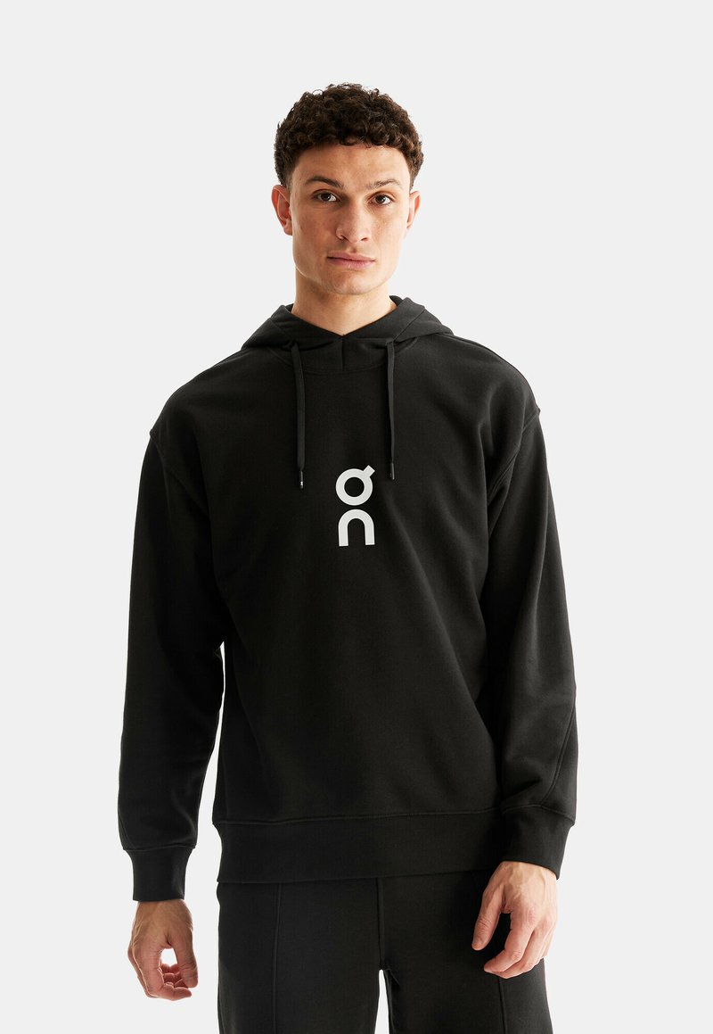 Zwarte hoodie van zacht materiaal, met een kangoeroezak en een groot contrasterend wit logo op de borst. Verstelbare trekkoordkap.