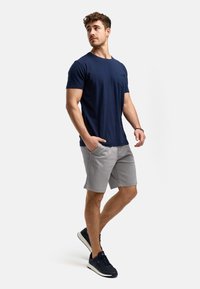 Granatowa bawełniana koszulka z kieszonką, zestawiona z jasnoszarymi szortami. Model ma na sobie granatowe sneakersy z białymi podeszwami. Prosty, codzienny strój.