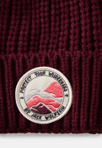 Gorro de malha cor bordeaux com um patch bordado redondo contendo montanhas, o texto "PROTEJA A SUA VIDA SELVAGEM" e o logótipo da Jack Wolfskin.