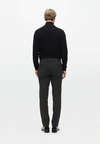 Maglietta nera a maniche lunghe, pantaloni grigi su misura, texture liscia, taglio dritto con tasche, indossata con scarpe nere, vista da dietro.