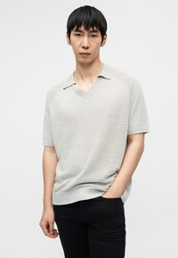 Ανοιχτό γκρι πουλόβερ με κοντά μανίκια, V-λαιμόκοψη και ριμπ τελείωμα. Διαθέτει υφή με ανάγλυφη όψη και χαλαρή εφαρμογή, συνδυασμένο με σκούρο παντελόνι.