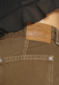 Ruskeat farkut, joissa on nahkainen Levi Strauss & Co. -merkki, hopeiset napit ja kontrastivalkoiset tikkaukset taskuissa.