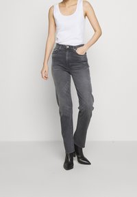 Gray high-waisted jeans with a straight-leg cut, worn with a fitted white tank top and black pointed ankle boots. Smooth denim texture.