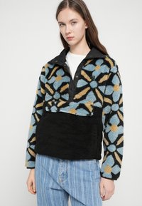 Φλις μπλούζα με μαύρο γιακά, με πολύχρωμο λουλουδάτο σχέδιο σε μπλε, κίτρινο και μαύρο, με μπροστινή τσέπη και υφή ύφασμα.