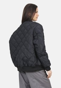 Zwarte gewatteerde bomberjack met een diamantpatroon, geribde manchetten en zoom, gemaakt van een soepele stof met een ontspannen fit.