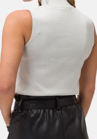 Haut sans manches gris clair avec un col montant et un léger éclat, associé à un pantalon en cuir plissé noir à taille haute avec une ceinture.