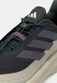 Εγγύς πλάνο μαύρου και γκρι αθλητικού παπουτσιού με τρεις ρίγες, υφασμένο πέλμα και κορδόνια σχοινιού δεμένα με μαύρο κούμπωμα και μοβ λωρίδα.