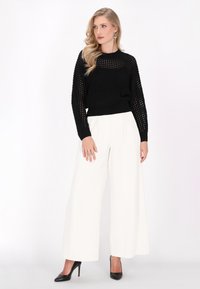 Zwarte gebreide trui met een textuurpatroon, gecombineerd met hoge witte wijde broek en zwarte stilettohakken.