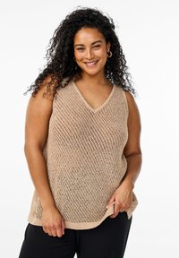 Beige pletený bezrukávový top s výstřihem do V, který má otevřenou texturu a volný střih, doplněný černými kalhotami. Žádné výrazné vzory ani akcenty.