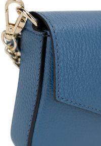 Angolo di una borsa a tracolla in pelle blu testurizzata con rifiniture nere, dotata di una chiusura in metallo dorato e dettagli di cucitura delicati.