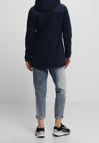 Marinblå huva jacka med strukturerad yta, kombinerad med ljusa denimjeans. Skorna har svarta och vita detaljer och är designade för komfort.