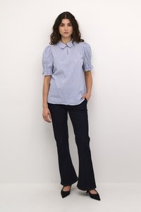 Blusa a maniche corte a righe azzurro chiaro e bianco con colletto, abbinata a jeans a zampa scuri e scarpe nere con punta. 