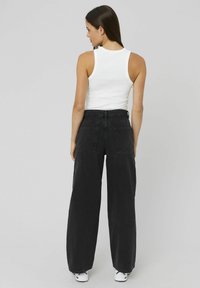 Jean large noir à taille haute, grandes poches arrières et coupe décontractée. Associé à un débardeur blanc ajusté et des baskets blanches.