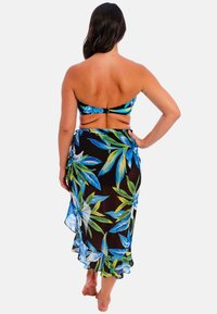 Top de bikini tipo bandeau con estampado floral tropical en azul y verde, combinado con una falda negra transparente con dobladillo con volantes.