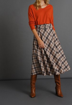 Roestkleurige V-hals trui gecombineerd met een geruite, knielange rok in beige, bruin en zwart, met een tailleband en bruine kniehoge laarzen met hak.