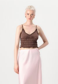 Rjav prilegajoč crop top z nabranim teksturo in nabranimi robovi, v kombinaciji z svetlo roza, satenskim krilom, ki ima sproščen kroj.
