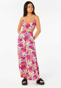 Robe maxi florale en rose, orange et jaune avec un détail noué à l'avant et des découpes à la taille, fabriquée dans un tissu léger. Sandales à plateforme noires.