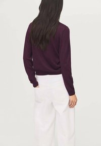 Suéter morado de manga larga, ajustado en la cintura, combinado con pantalones de pierna ancha de cintura alta blancos, de textura suave y con detalles mínimos.