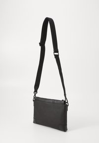 Black crossbody bag with a textured fabric body, smooth leather accents, adjustable strap, and zippered closure. Rectangular shape.
