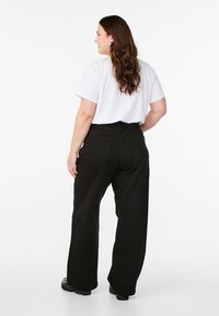 Mustat leveälahkeiset farkut, joissa on takataskut ja korkea vyötärö, yhdistettyinä valkoiseen t-paitaan, nähtynä takaa.