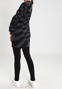 Un vestido suéter de patrón negro y gris con mangas largas, un ajuste ceñido y un diseño geométrico, combinado con leggings negros y zapatillas blancas.