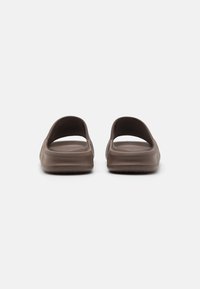 Brune slidesandaler med åbne bagsider, lavet af glat materiale. Har en tekstureret sål og et minimalistisk design uden udsmykninger.