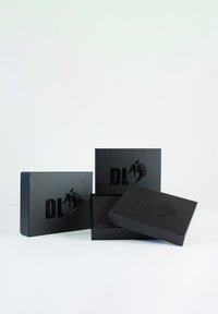 Boîtes cadeaux noires avec une finition mate, présentant un logo "DL" en relief et un logo de licorne. Différentes tailles, dont une ouverte pour révéler un intérieur noir.