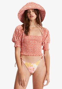 Top cropped floral vermelho com mangas bufantes, combinado com um biquíni estampado em rosa e amarelo. Ambos os itens possuem laços ajustáveis.