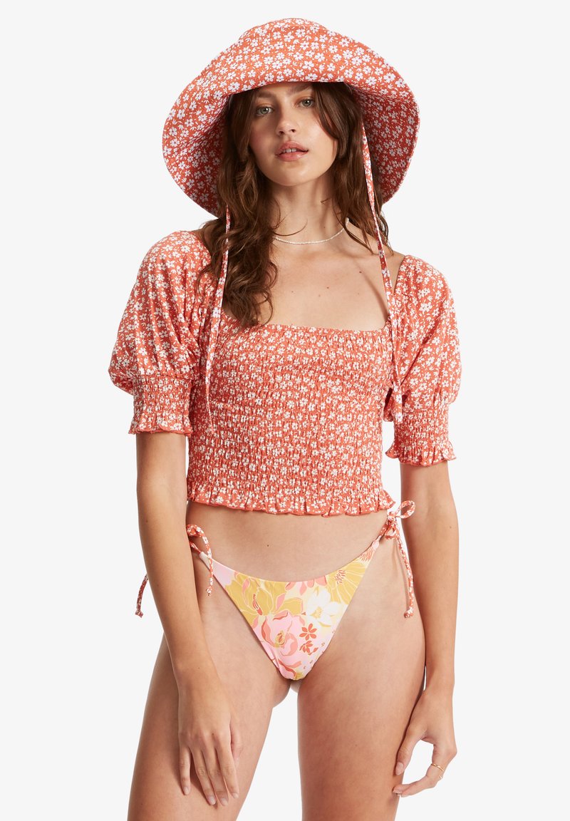 Top cropped floral vermelho com mangas bufantes, combinado com um biquíni estampado em rosa e amarelo. Ambos os itens possuem laços ajustáveis.