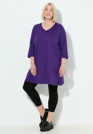 Paarse V-hals tuniek met driekwartmouwen, zijsplitten, gecombineerd met zwarte leggings en chunky zwarte schoenen. Gladde stofkwaliteit.
