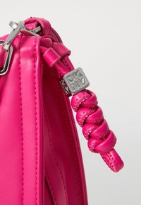 Ροζ δερμάτινη τσάντα χειρός με κομψό σχέδιο, λεπτομέρεια πλεξίματος στη λαβή και μεταλλικό λογότυπο DKNY σε ασημί απόχρωση. Υφή με ραφές.