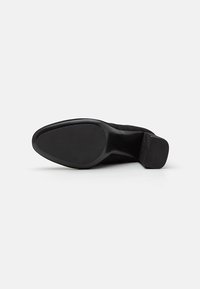 Scarpa nera in suede con tacco alto, punta affusolata e suola testurizzata. Presenta un tacco a blocco nero solido per maggiore stabilità.
