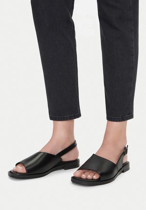 Sandale negre din piele cu toc deschis și talpă joasă, plată. Au cataramă și o textură netedă.