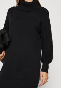 Robe col roulé noire avec manches en maille texturée. Matière douce et côtelée ; coupe décontractée ; dotée d'un col montant et d'un ourlet droit.