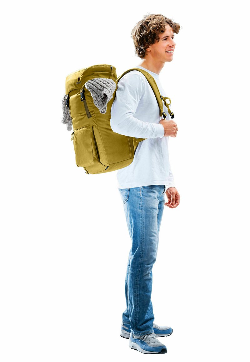 Gelber Rucksack mit mehreren Reißverschlusstaschen und Clips, grauer Pullover liegt oben drauf, getragen von einer Person in legerer Kleidung.