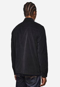 Camicia di velluto a coste nera con colletto bottonato e maniche lunghe. Presenta una texture liscia e un design leggermente rilassato.