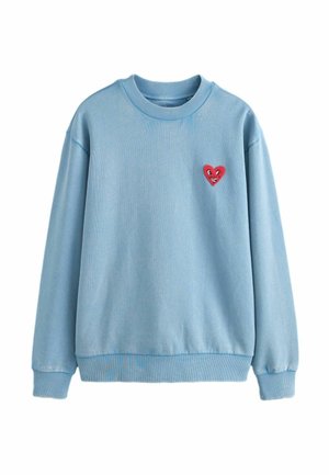 Vaaleansininen pyöreäkauluksinen collegepaita, jossa on resorit hihansuissa ja helmassa. Vasemmassa rinnassa pieni punainen sydänmerkki, jossa on hymyilevä kasvot.