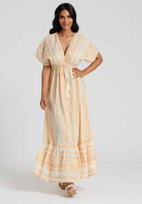 Robe maxi légère en crème avec des rayures verticales oranges et un ourlet à volants. Présente un décolleté en V, des manches courtes et un accent de taille à cordon.