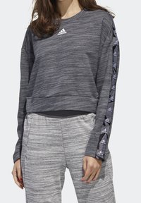 Camiseta atlética gris de manga larga con tejido texturizado, que presenta un cuello redondo y franjas laterales negras contrastantes con el logo de Adidas.