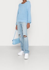 Jasnoniebieski sweter z dzianiny o okrągłym dekolcie, w połączeniu z jasnoniebieskimi dżinsami z przetarciami i białymi, masywnymi sneakersami. Mała niebieska torebka dopełnia całość.
