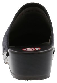 Schwarzer Clog mit gebogenem Rücken, Obermaterial aus strukturiertem Stoff und einer glatten, glänzenden Plattformsohle, die ein rundes Logo in Rot und Weiß aufweist.