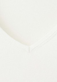 Tissu blanc doux à col en V, texture finement côtelée et détail de couture subtil au centre de l'encolure.