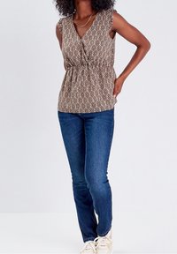 Haut sans manches brun à motifs avec un col en V et une taille froncée, associé à un jean bleu et des baskets claires.