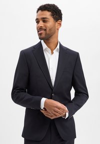 Marineblauer Blazer aus glattem Stoff. Ausgestattet mit einem Reverskragen mit Kerbe, Einzelknopfverschluss und Pattentaschen. Kombiniert mit einem weißen Hemd.