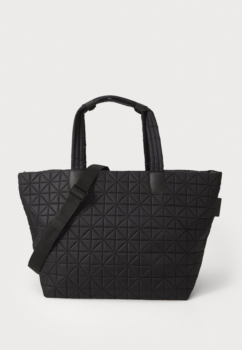 Svart quiltet tote bag med et teksturert triangelmønster, doble håndtak og en justerbar stropp, med stilige svarte akenter.