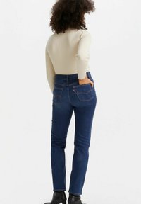 Jeans ajustados de denim azul oscuro con una textura suave, cintura alta, dos bolsillos traseros y detalles de costura en contraste.