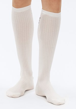 Stehenné pančuchy s rebrovaným vzorom v svetlej béžovej farbe, vyrobené z mäkkého materiálu. Bezšvová špička a elastický lem pre pevné uchytenie.
