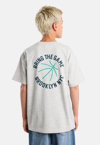 Gray cotton T-shirt features a round graphic with text "BRING THE GAME BROOKLYN NYC" and a green basketball design on the back.