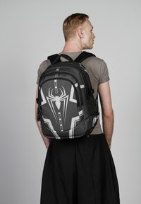Sac à dos sur le thème de Spider-man, noir et gris, avec un motif hexagonal, un logo de spider bien en évidence, plusieurs compartiments et des bretelles réglables.